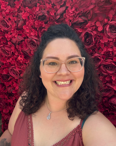 Front facing headshot of Stephanie wearing a blush dress standing in front of a red rose background.