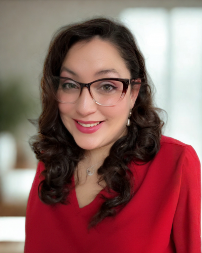 Front facing headshot of Alicia De Vargas wearing a red blouse with a blurred background